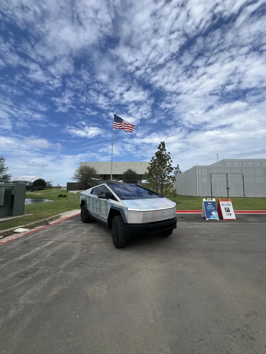 Skipper Cybertruck parked by a flagpole under big clouds