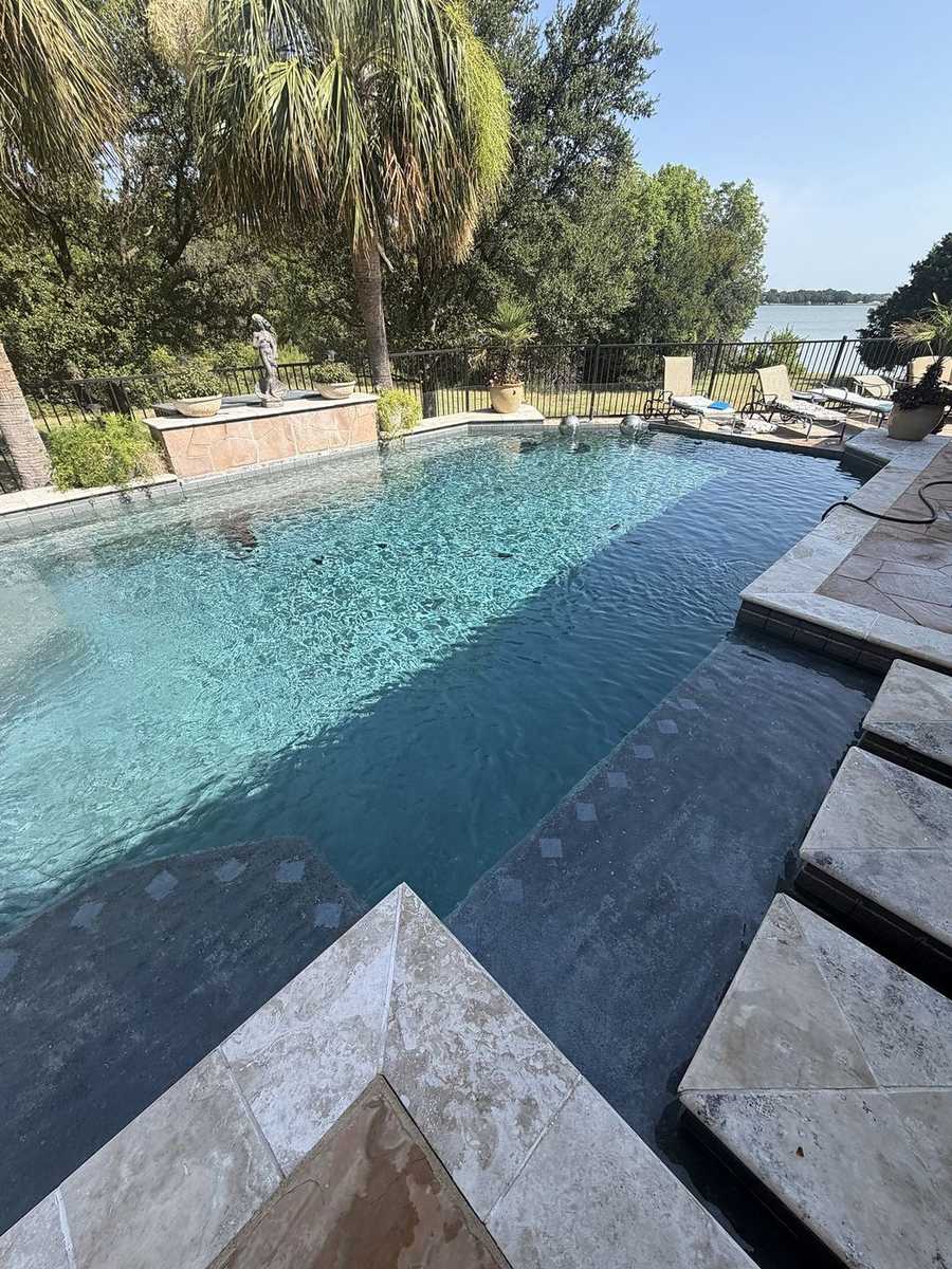 Clear pool with tanning ledge, palms, and a lake view