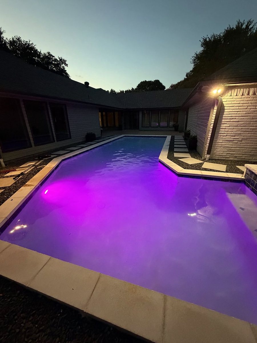 Rectangular pool glowing purple under night lighting at dusk
