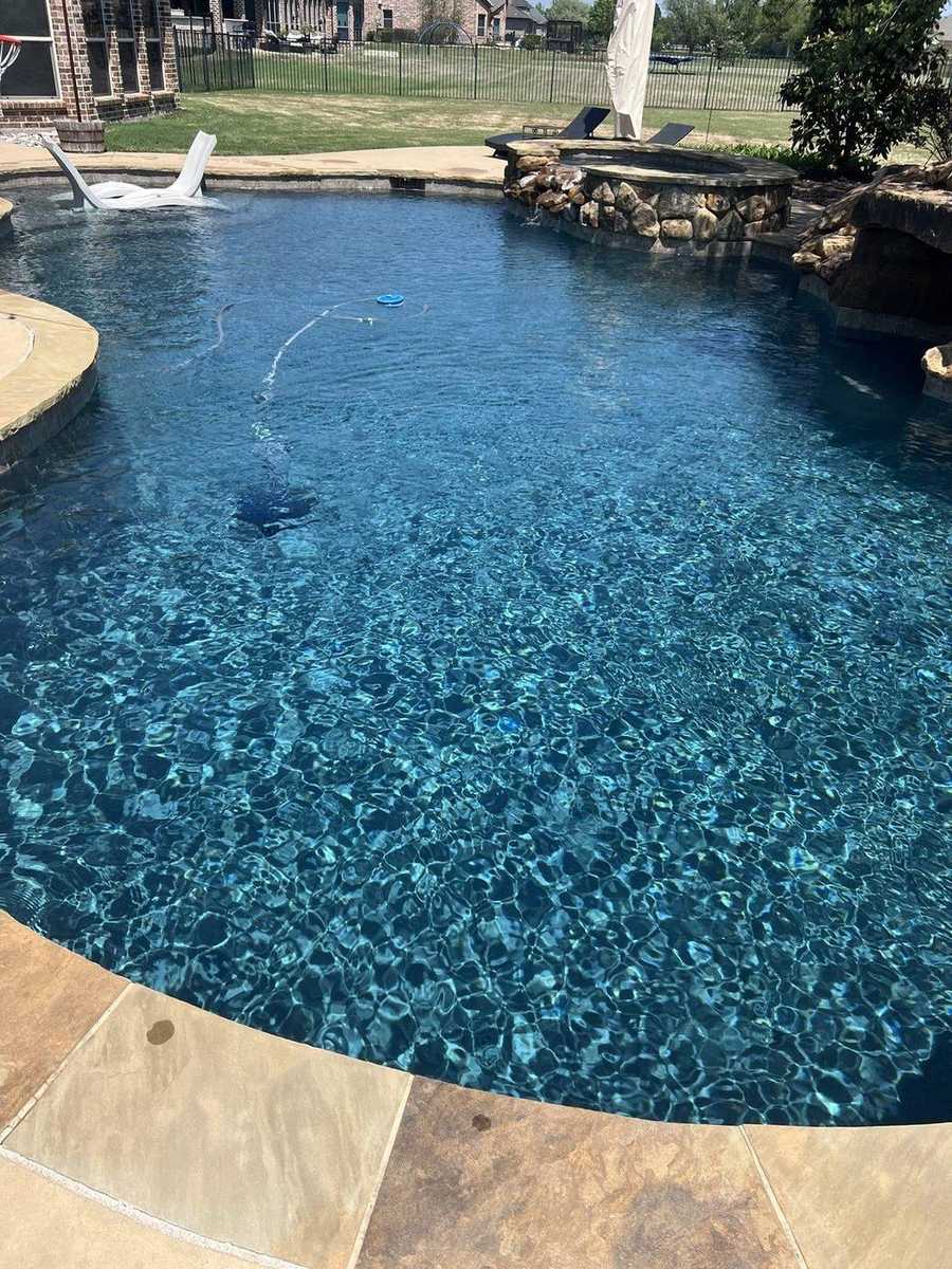 Teal freeform pool with stone spa and sun shelf lounge chairs